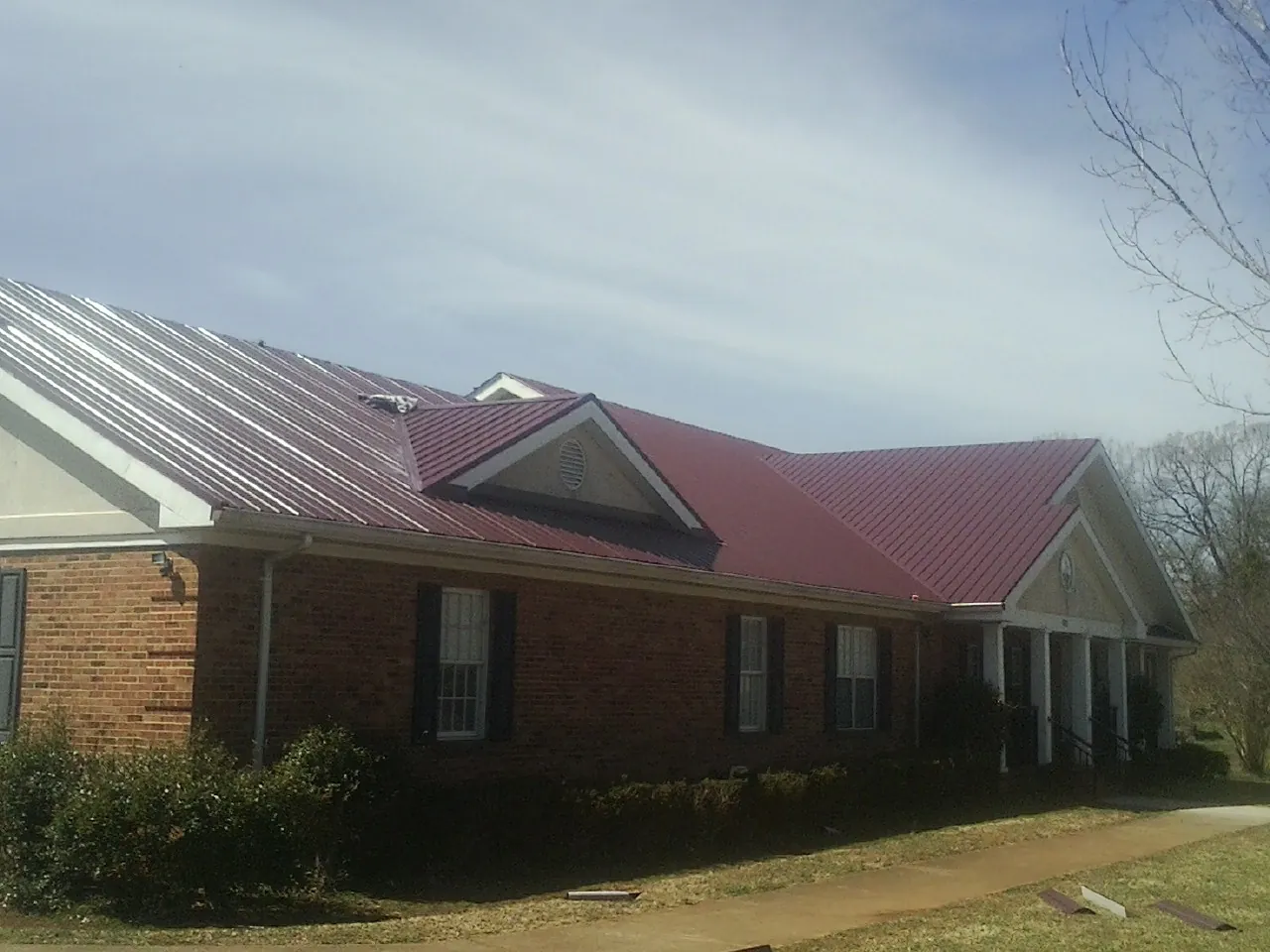 Red metal roof with gabled entries on a long brick building, from a Hail Damage Roof Repair job in Talking Rock