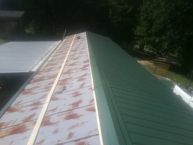 Old rusted panels beside newly installed green metal roofing — Wind Damage Roof Repair by Roofing Brothers in Talking Rock