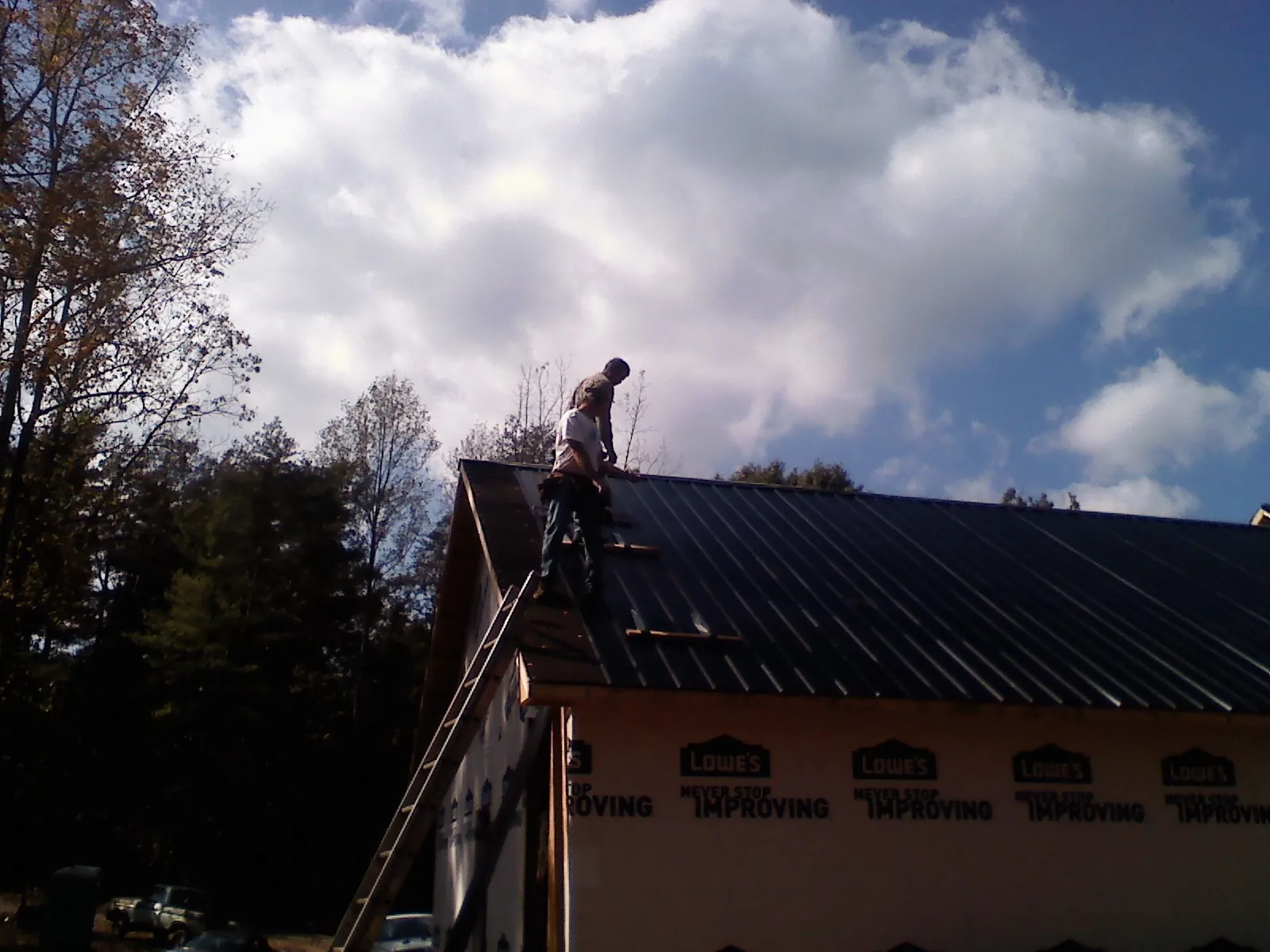 Roofer fastening dark metal panels high against a cloudy sky, from a Roof Inspection job in Talking Rock