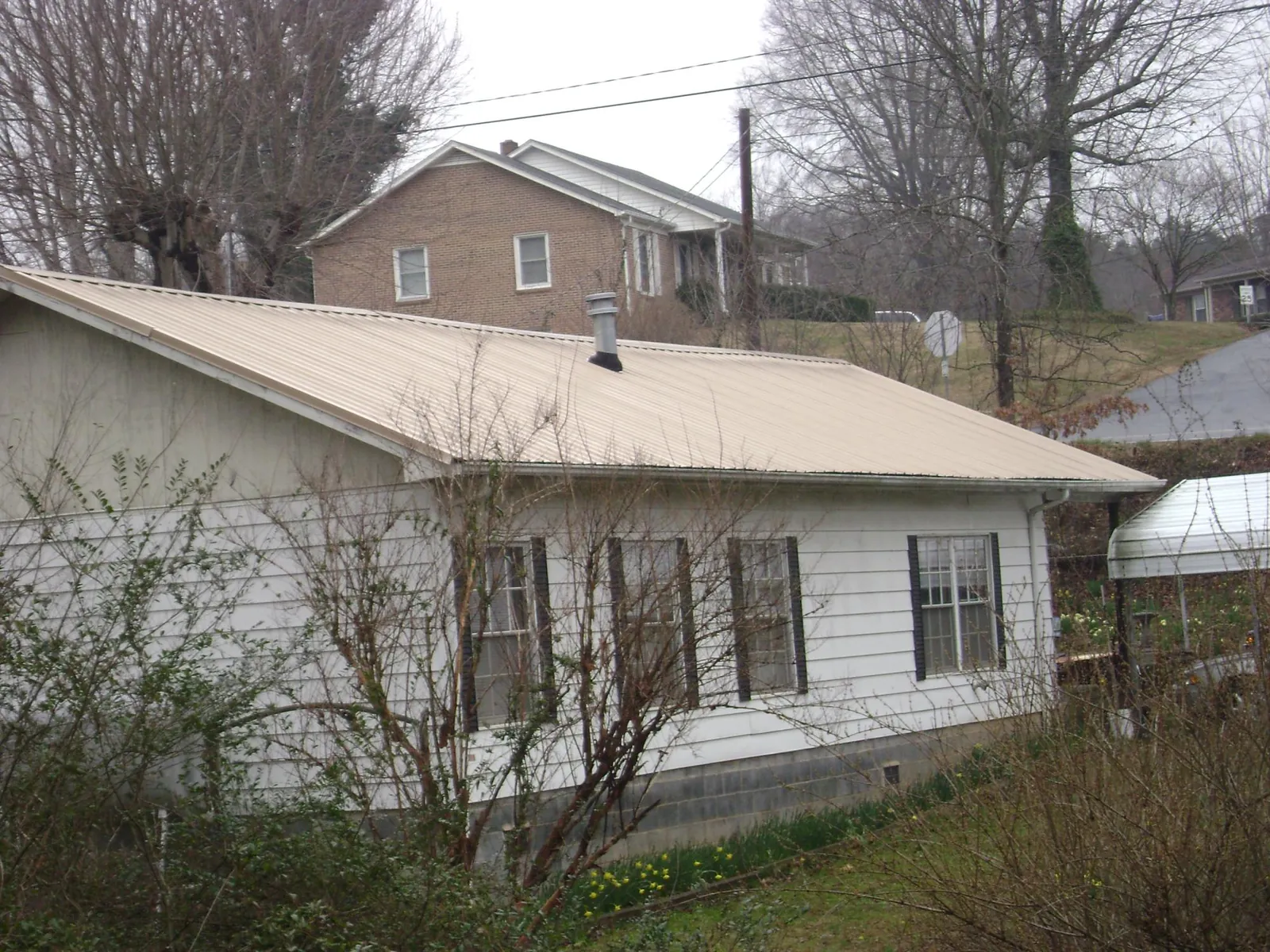 Tan metal roof on a white sided house set into a hillside — Commercial Roofing by Roofing Brothers in Talking Rock