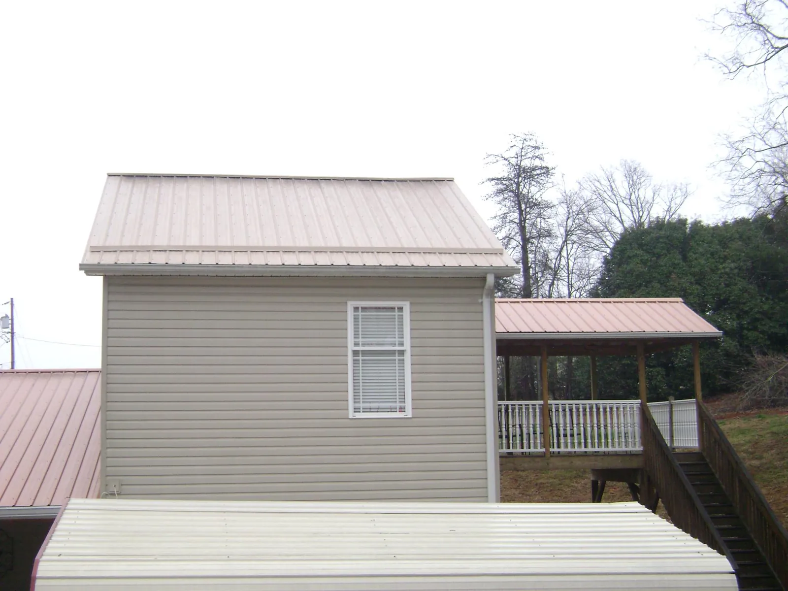 Tan metal roofs on a two story addition and attached porch, from a Roof Replacement job in Talking Rock